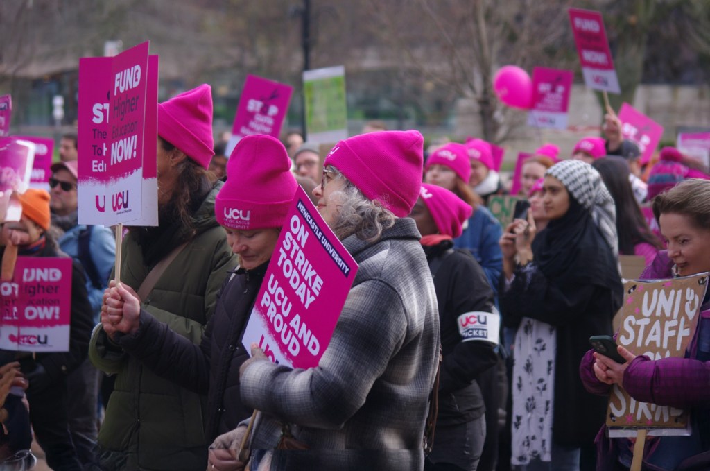 Newcastle University employees on a picket line, wearing and carrying UCU beanie hats and placards
